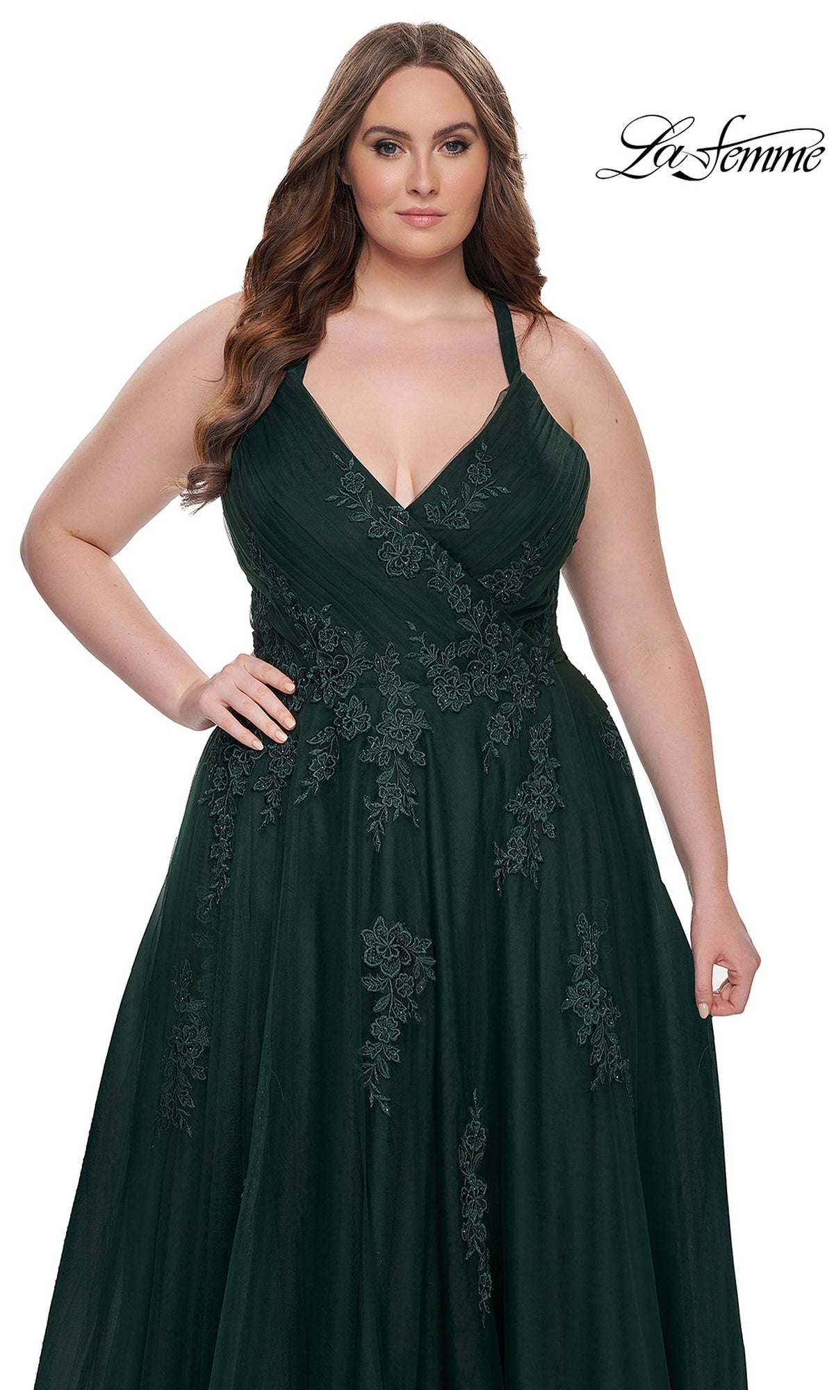 A woman wears the La Femme Long Prom Dress 29021, a dark green, sleeveless ball gown with floral lace detailing, fitted bodice, and flowy floor-length skirt, standing against a white background.